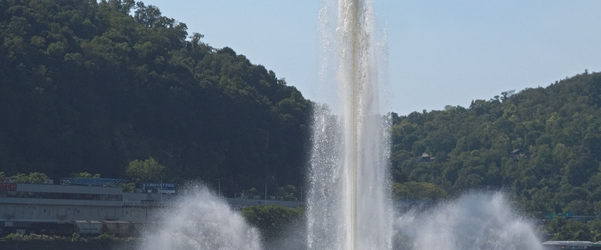 The tall fountain at Point State Park spraying water in front of green hills on a sunny day