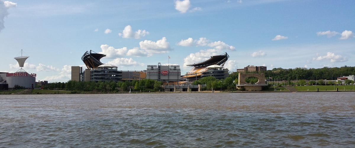 The North Shore football stadium seen from across the wide river on a sunny day with puffy clouds